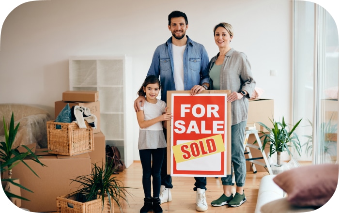 Two young homeowners with the 'sold' sign from their property.